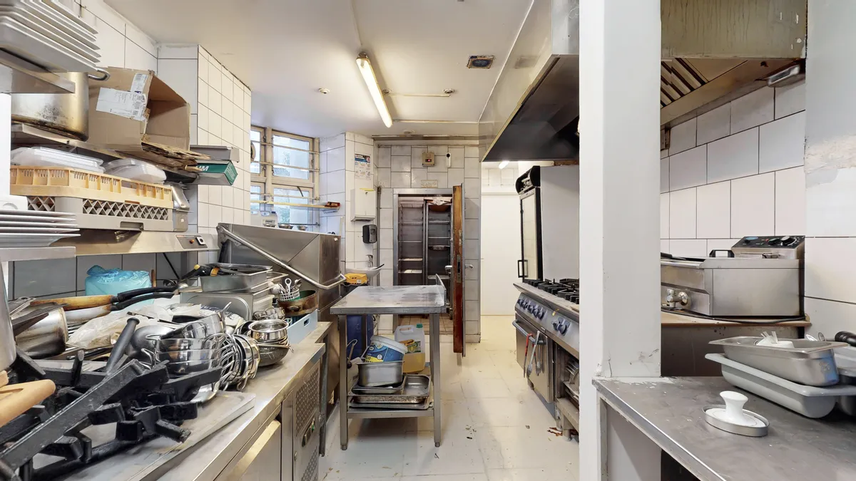 Køkken med apparater og tallerkener, stålborde og -hylder samt udstyrede kogeapparater og ovne for restaurantforretning