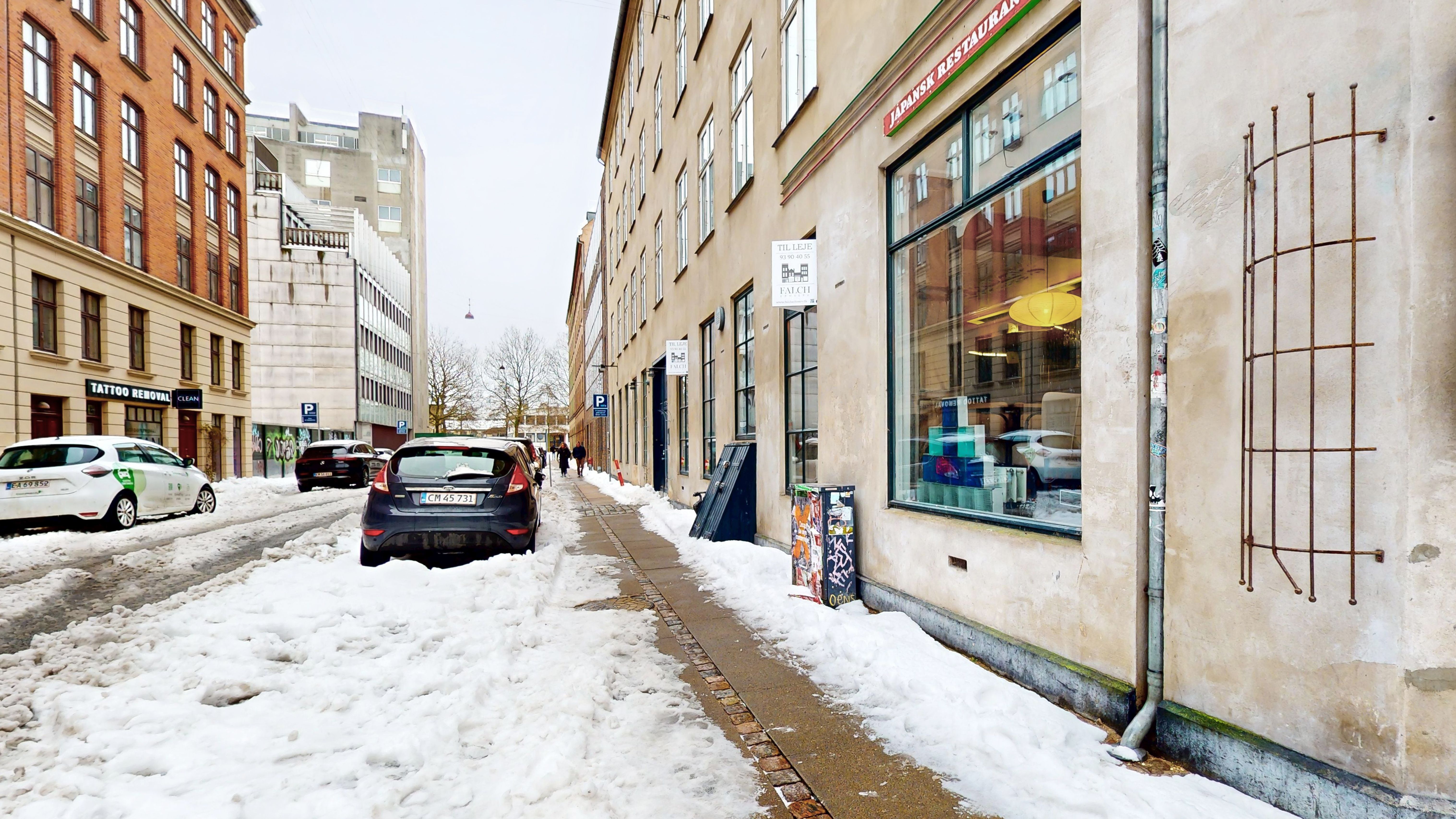 Sneede dækker gaden og bygningerne med mange biler parkeret på snedækket og folkene går forbi en bygning med en skilt og et vindue med udsigt