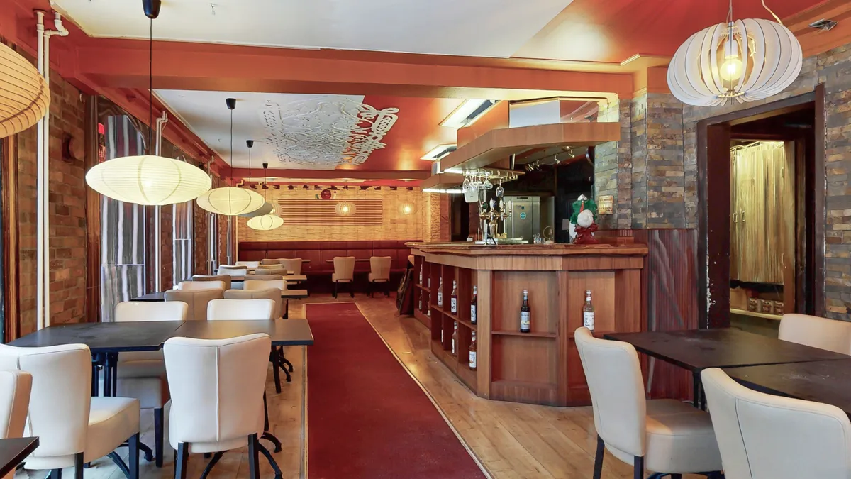 Lyse hvide læderstole og bord med rødt løbebånd og lyse lamper og lysegul træbar i et spisestueområde i et restaurantlejemål