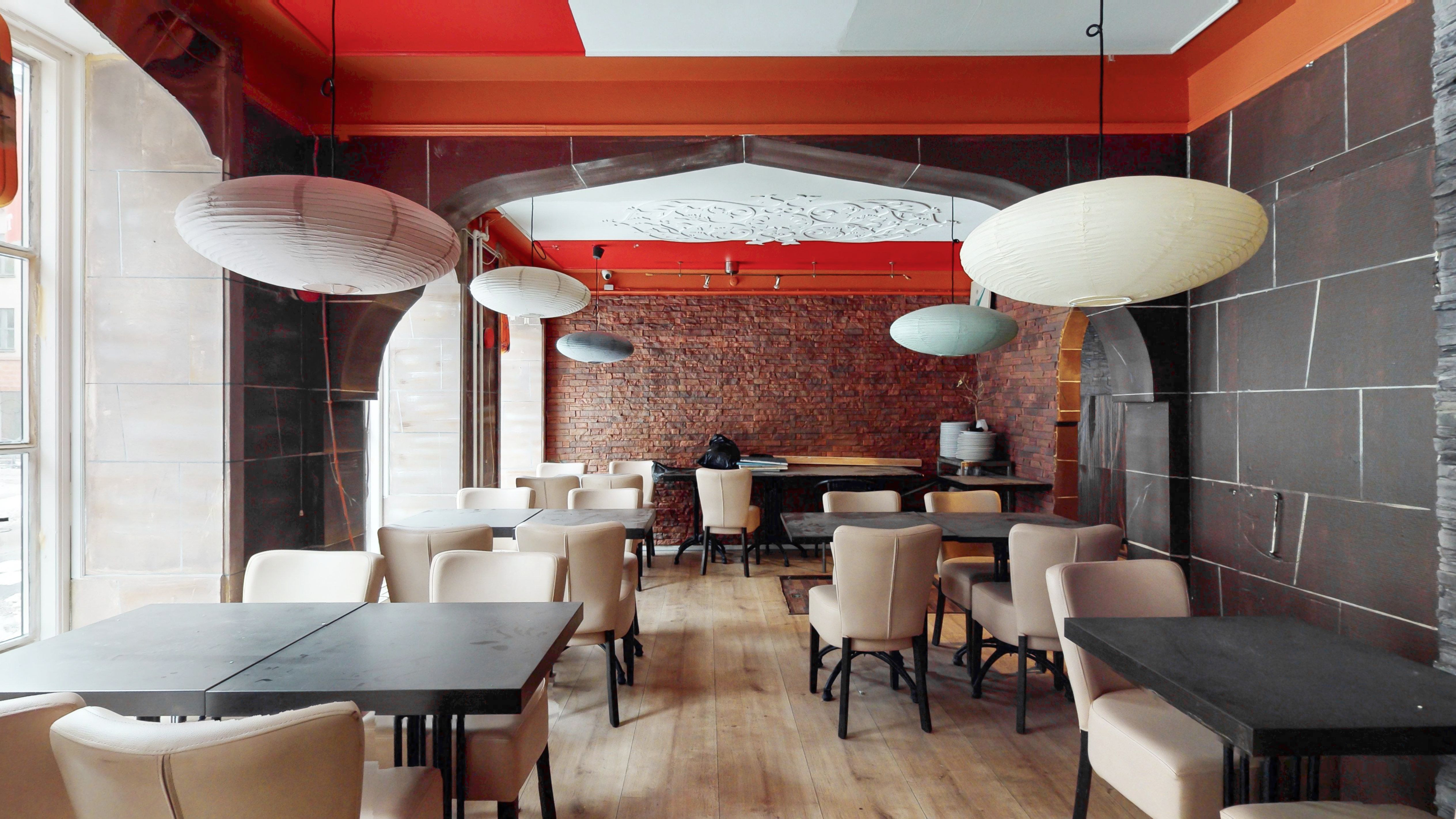 Rummeligt erhvervslejemål med lyse loftslampe og trægulve, møbler og borde samt røde og hvide vægge