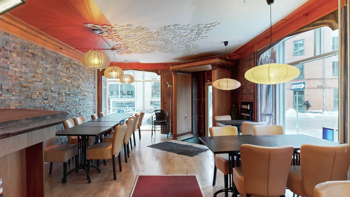 Indvendigt restaurantområde med trægulve, lysekroner, sofaer og borde med stole samt udsigt til gaden gennem store vinduer med skilte
