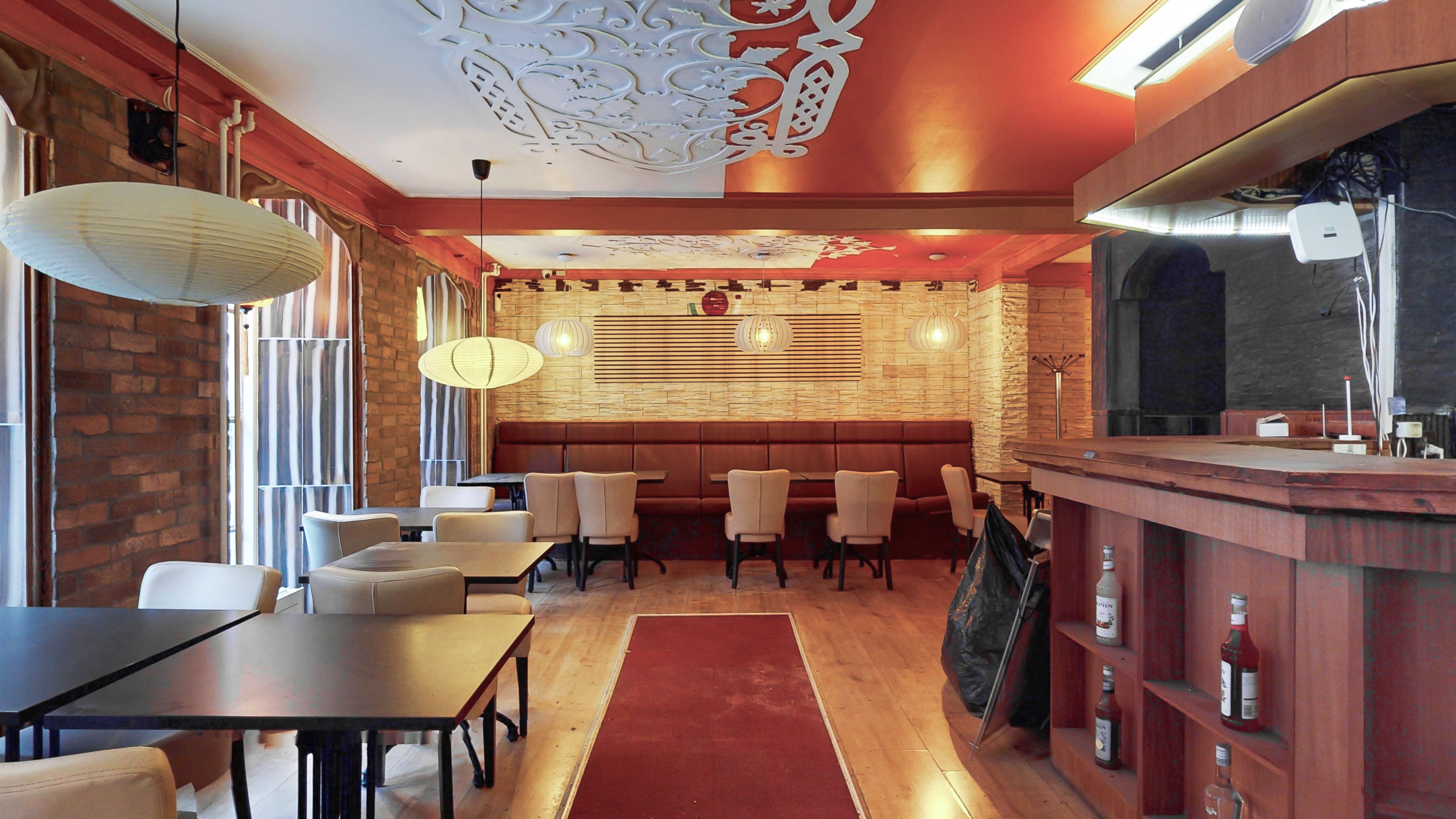 I stueetagen er der et stort, moderne restaurantområde med beige stole og borde samt en bar med lyse puder og træhylder med drikkevarer