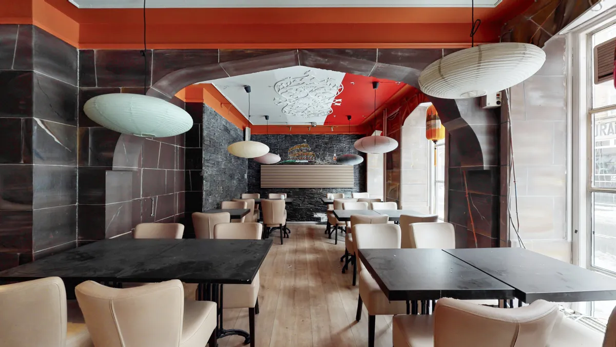 Moderne restaurant med røde vægge, hvide loftslamper, lyse beige stole og lysegrå trægulve