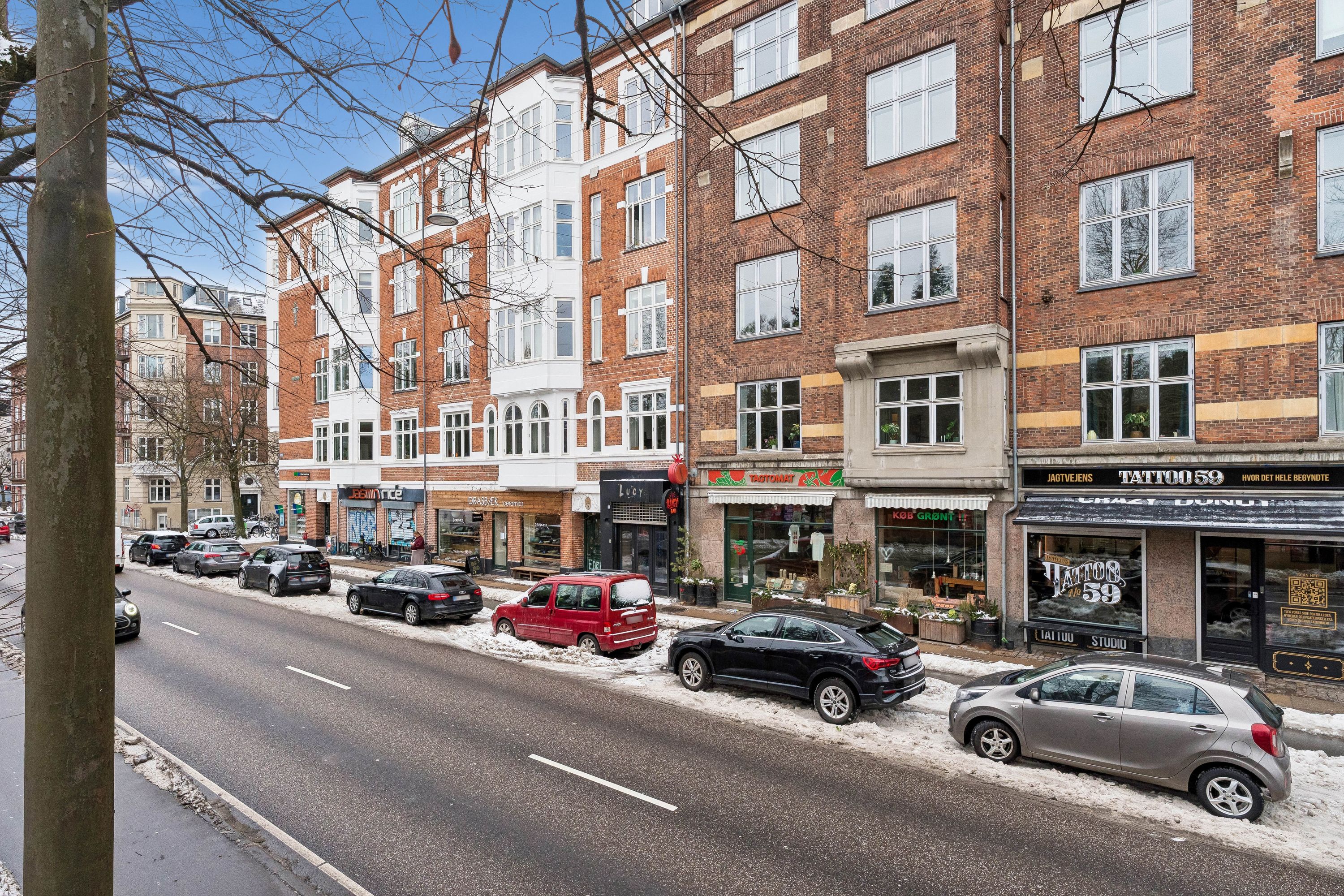 Forskellige biler er parkeret på Jagtvej med snedækket, og nogle forretninger har skilte med navne som Jagtvejens og Tattoo 59