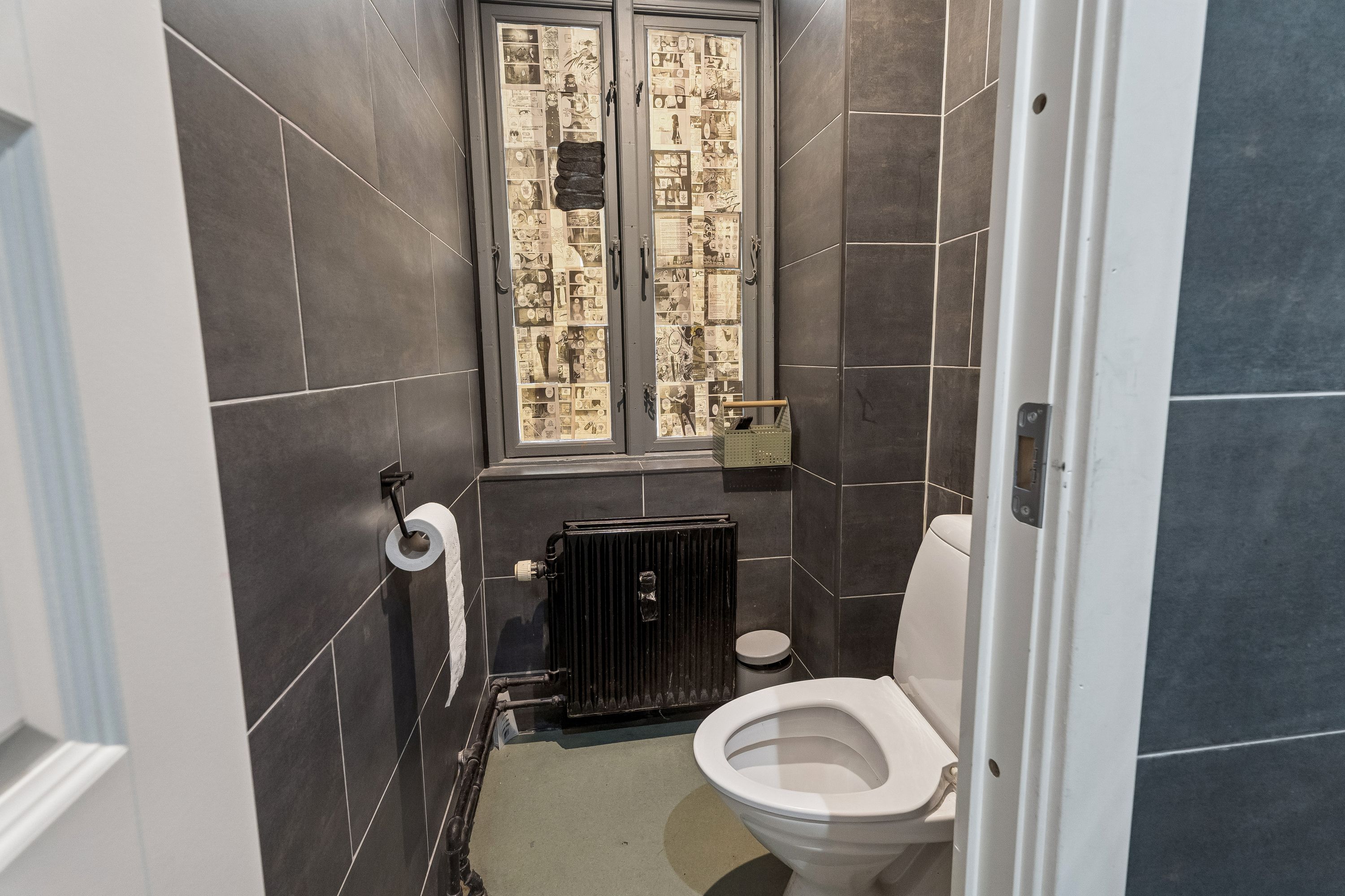 En moderne og veludstyret toiletrum med hvide vægge, en hvid toilet med åben dør, toiletpapir og en radiator i hjørnet, og en spejltørrer med to tørklæder