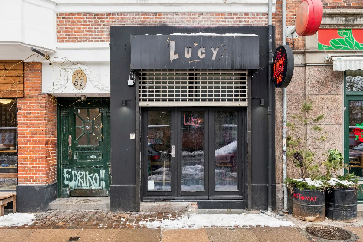 Velkendt bar med navnet Lucy på Jagtvej 57, København. Indgangsdør med glas og lysestage samt snedækkede plantefade. Siden er udsmykket med graffiti og en skilt med Lucy Bar.