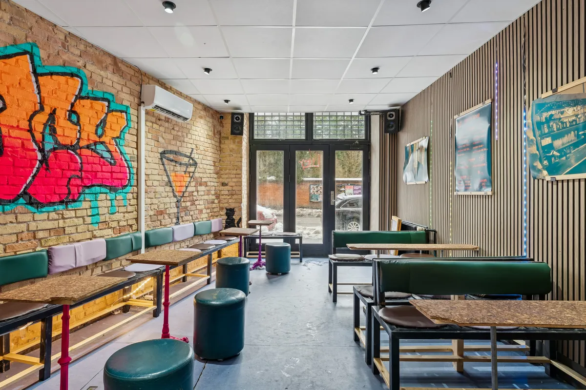 En moderne bar med graffitivæg, stolpeborde, høje stole og store vinduer, der skubber ud mod en bilparkering