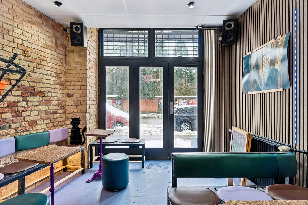 En lejet bar med grønne stole og borde samt møbler og lysanlæg i en bygning med krydsfinerbeklædte vægge og udsigt til en snefyldt vej