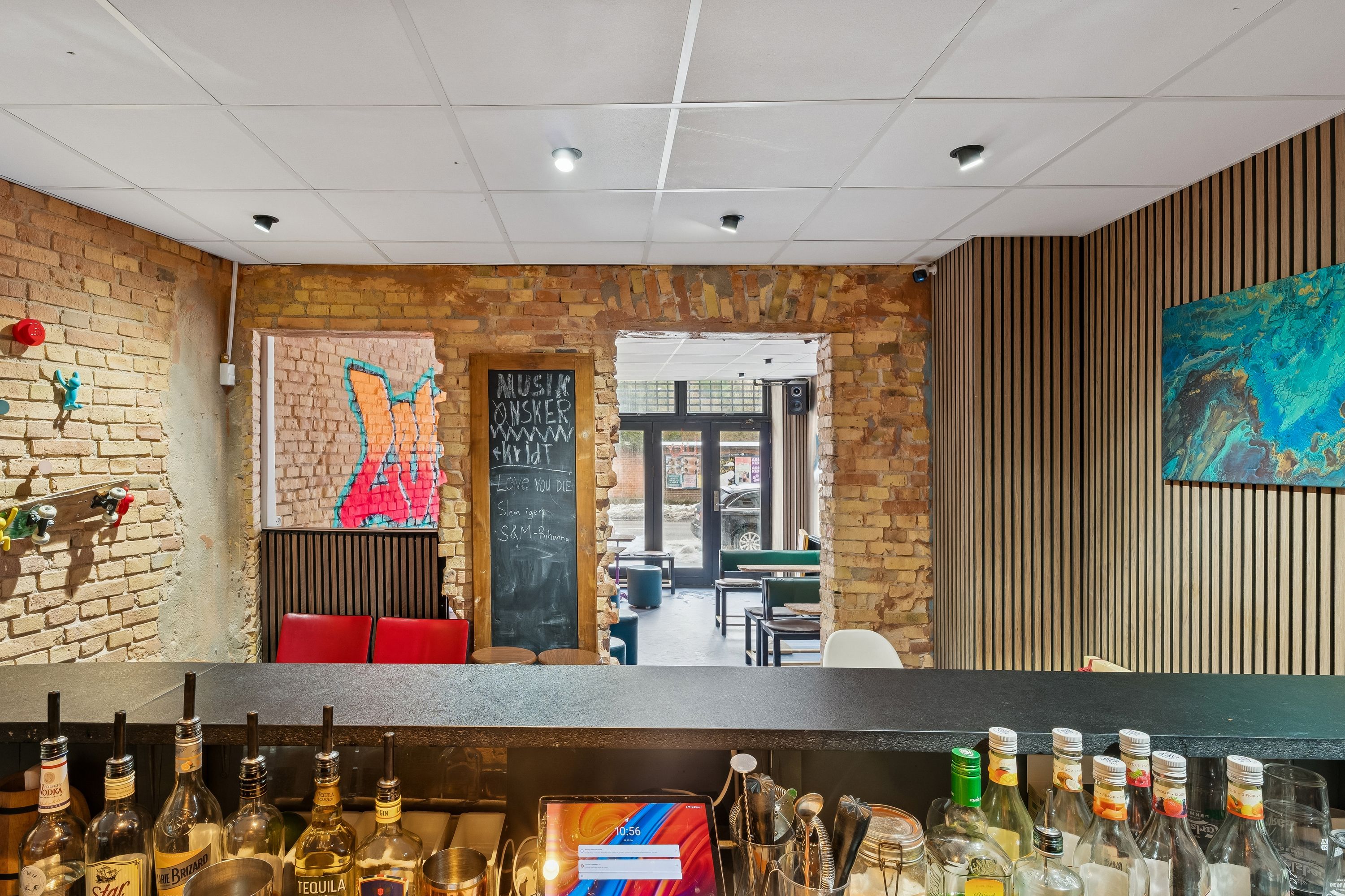 En bar med et stort udvalg af spritflasker og glas på baren samt en menutavle og malerier på væggen