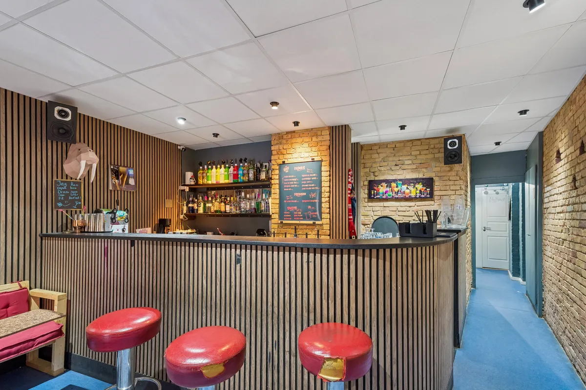 Bar til leje med cocktailbar, røde stolpebarer og træpaneler på Jagtvej 57 i København N. Sort menutavle, ølflasker og udsmykning.