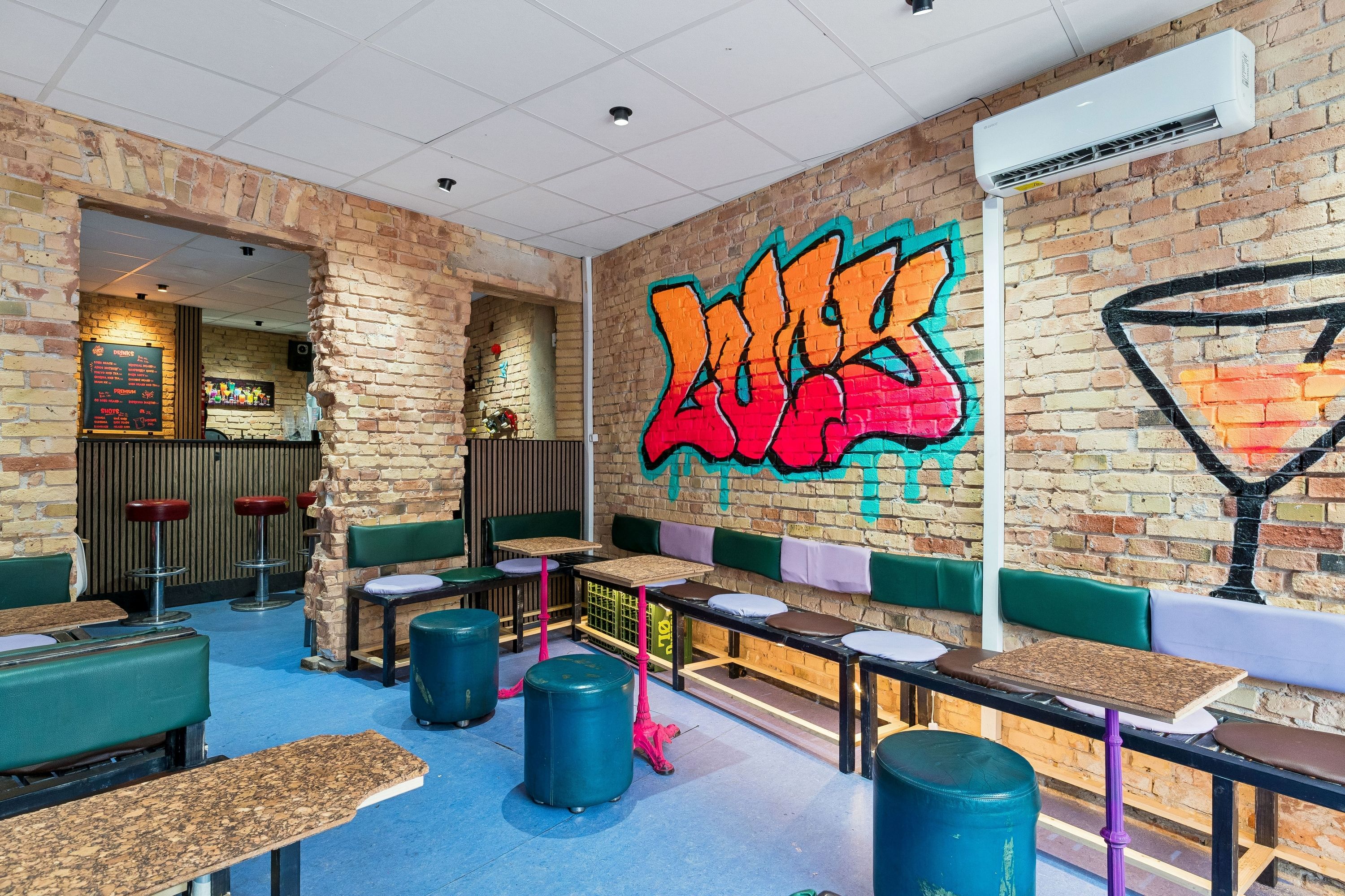 Inde i en bar med graffiti og røde stole samt runde gule og røde stole med træborde og høje stole