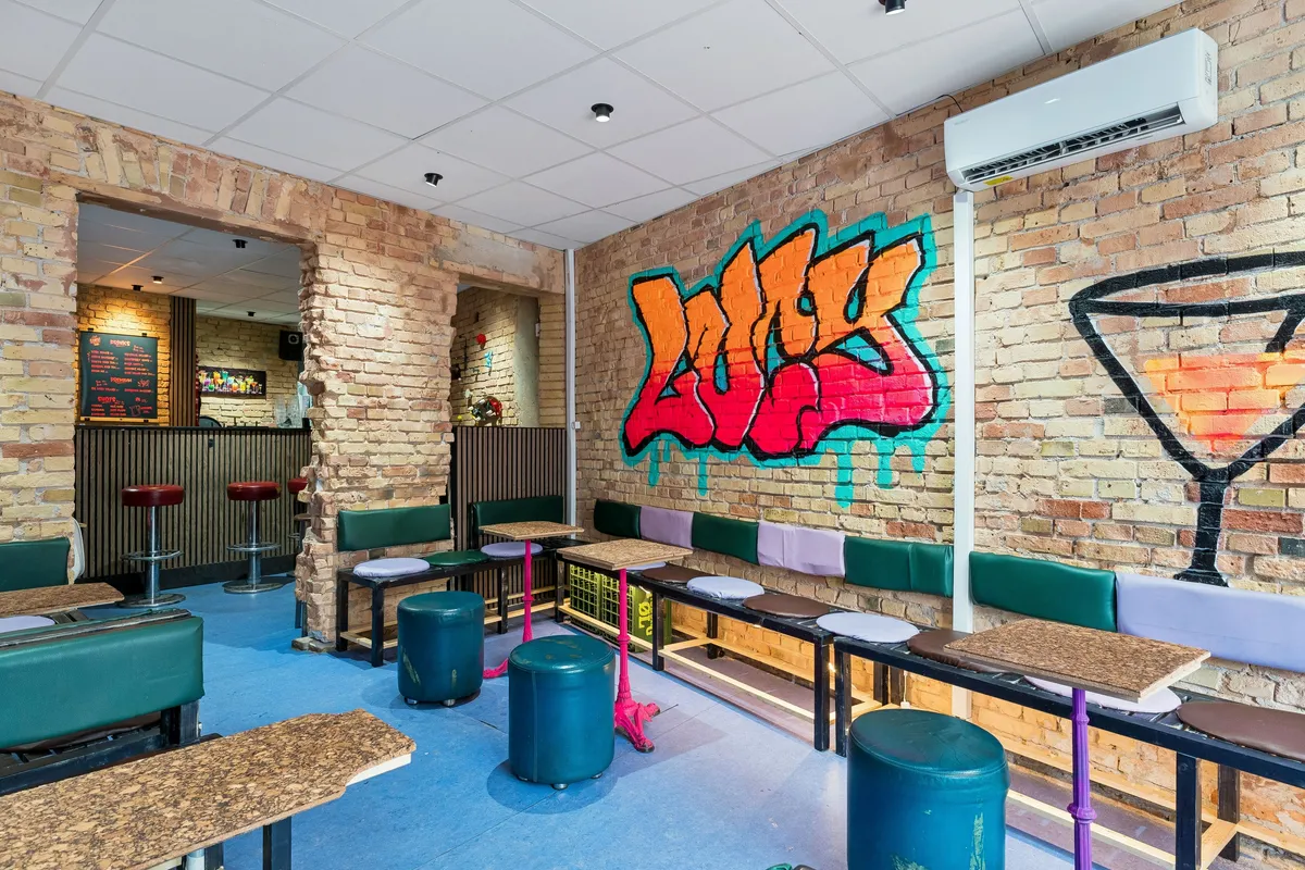 Inde i en bar med graffiti og røde stole samt runde gule og røde stole med træborde og høje stole