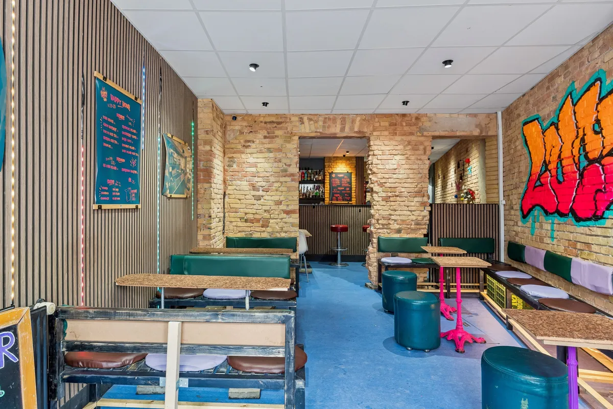 Bar til leje med grønne stole og borde, graffiti på væggen, loftslys og gul gulvbelægning i København