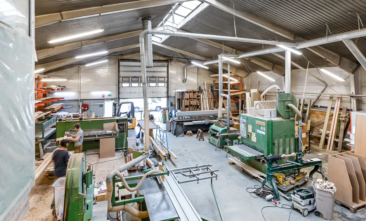 Et stort værksted med maskiner og værktøj. To mænd arbejder med maskineri. Værkstedet er udstyret med diverse udstyr og materialer.