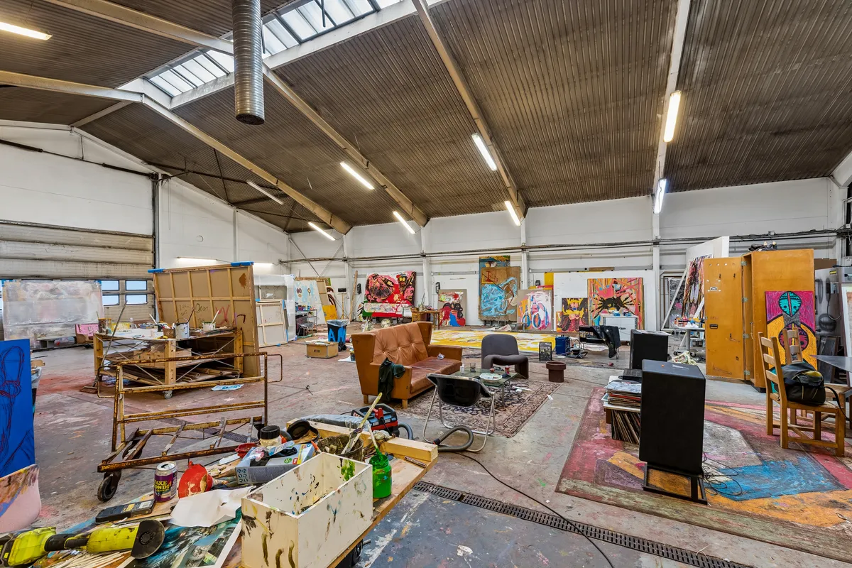 Malerværksted med flere store malerier og værktøj i en stor lejehal med højt loft og store vinduer