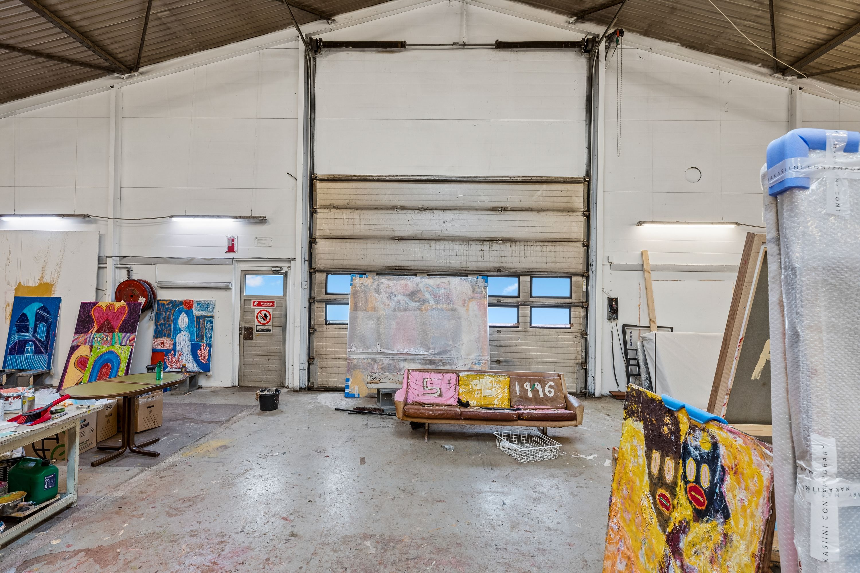 Store kunstværker er opstillet i et stort rum med høje lofter og store ruder samt en stor garagedør