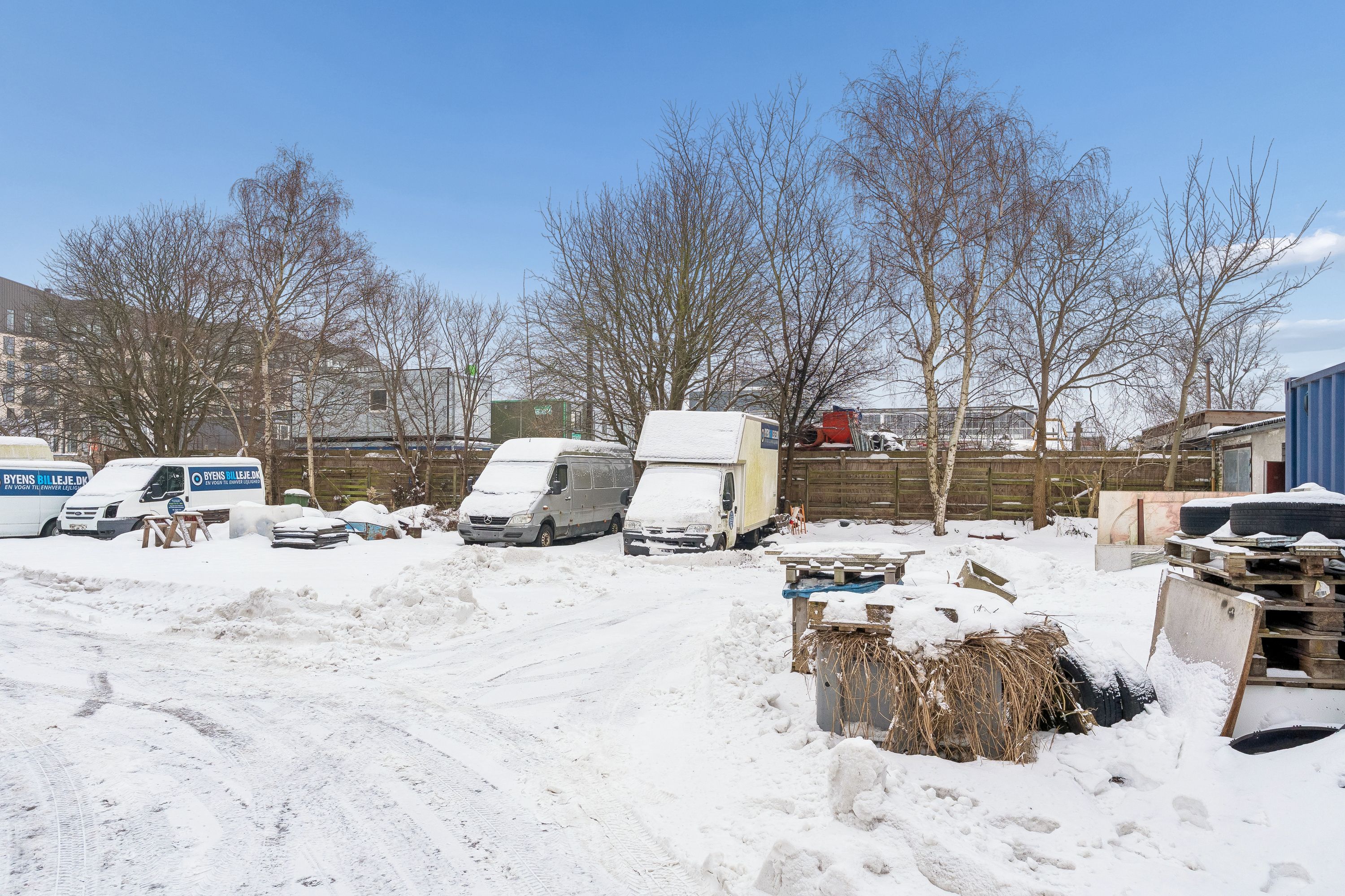 Sneede vej med fire parkerede lastbiler og forskellige genstande og affaldscontainere i baggrunden