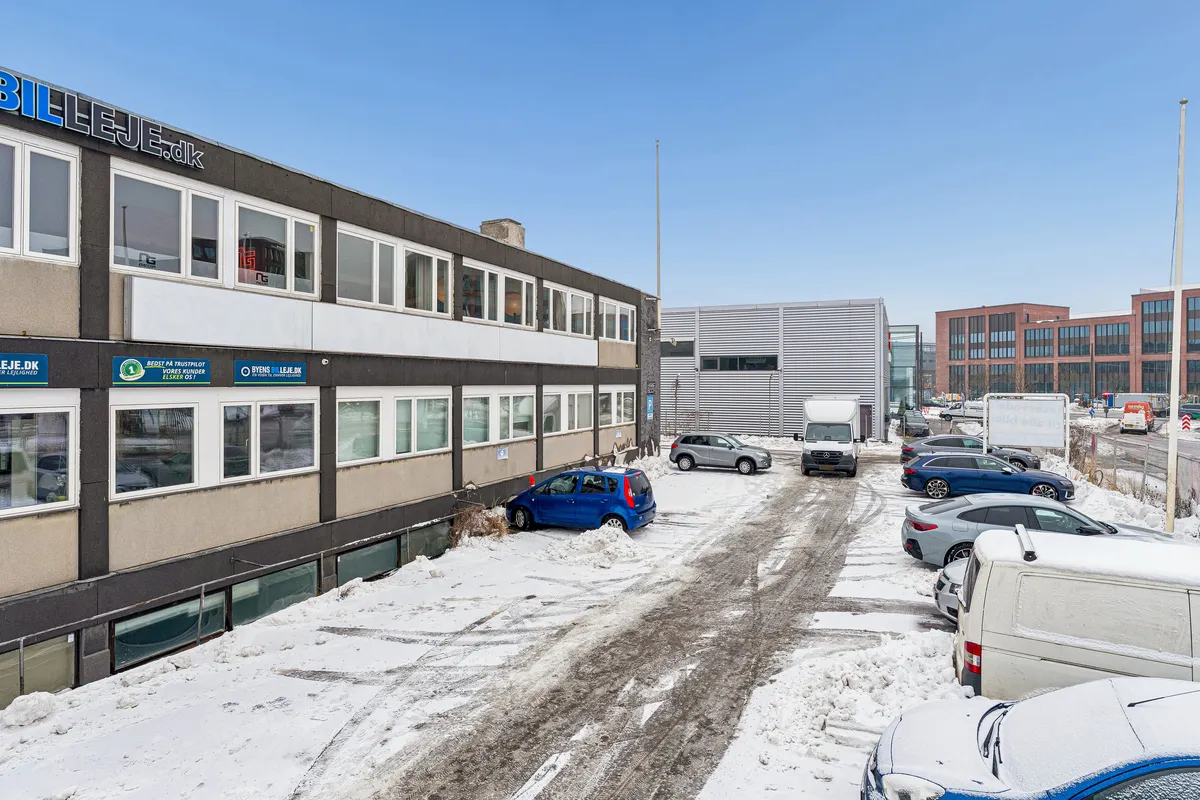 Forretningslokaler i København SV med bilparkering foran og sne på jorden. Parkerede biler og læssevogn er synlige på baggrunden