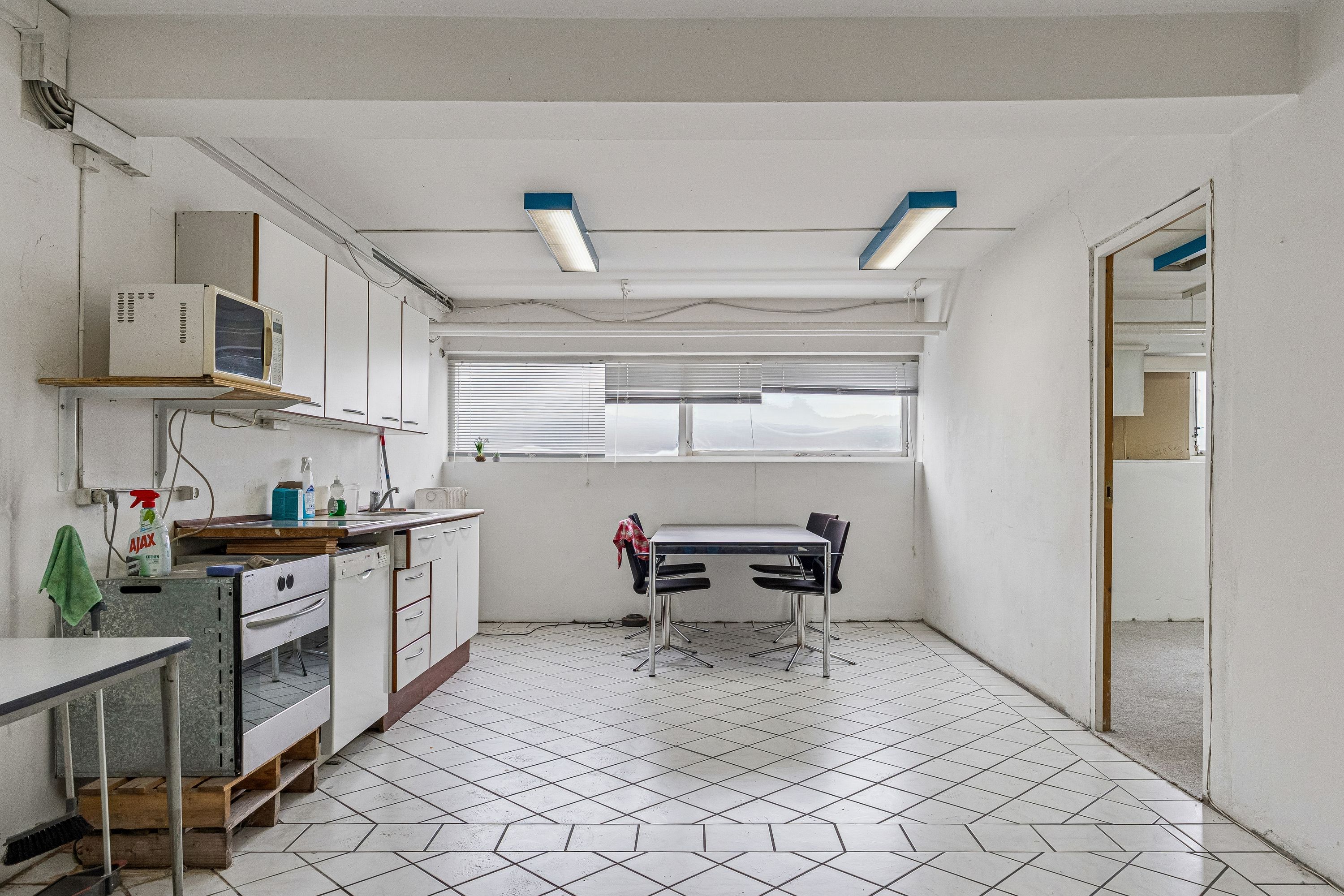 Lyst kælderlejemål med højt loft og køkken med ovn og mikrobølgeovn på Bådehavnsgade i København SV. Funktionelt køkken med bord og stole samt opvaskemaskine.