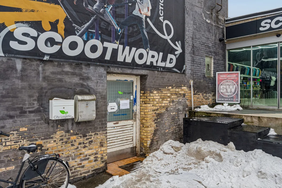 Lejlighed med lagerrum og personlig indgang i kælderen. Plakat med Scootworld og City Logistic samt scooter. Trapper med sne og reklameskilt med Trick Labenhul.