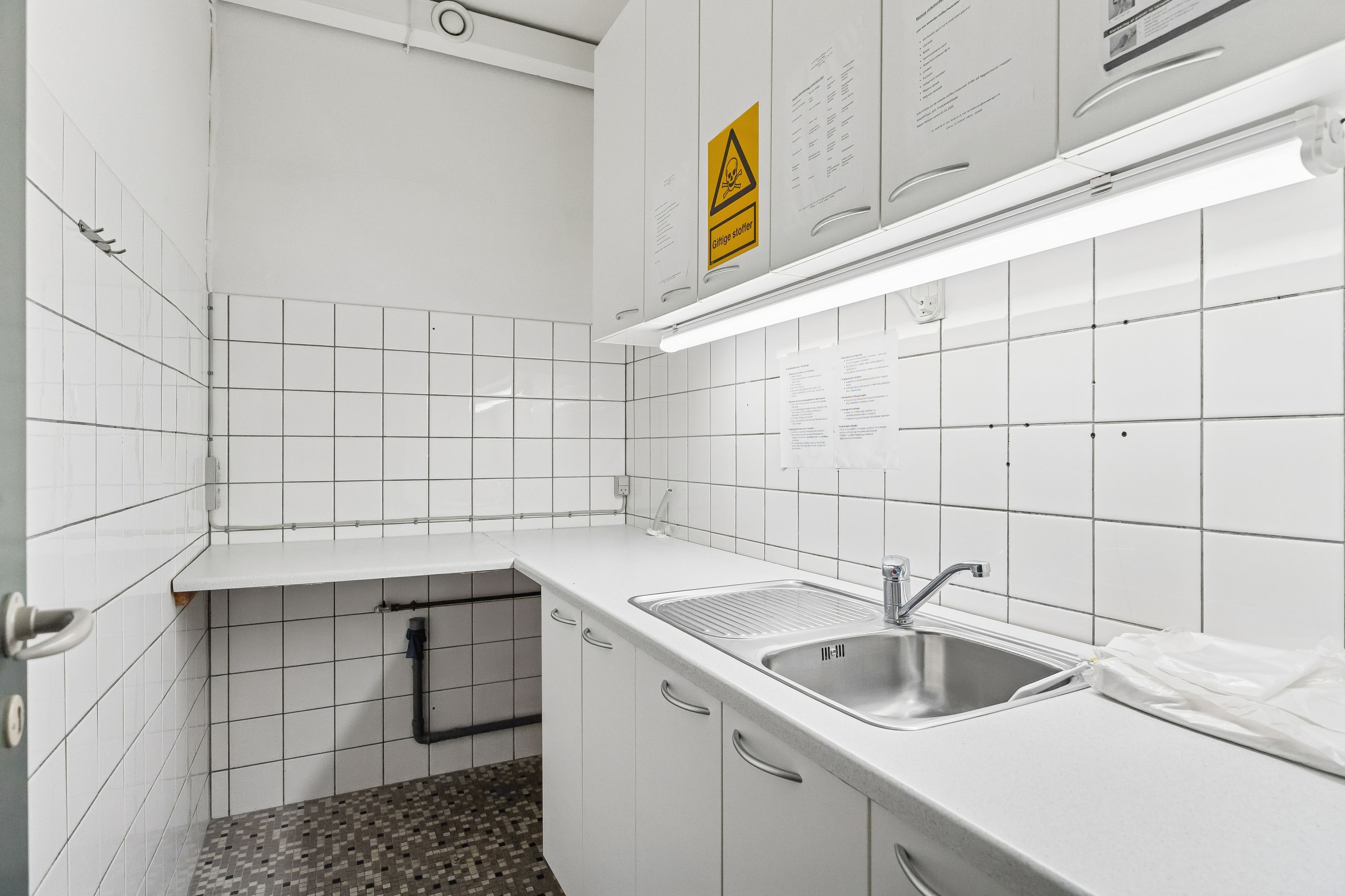 Rent og funktionelt køkken med hvid flise og lyseskabe, lyseblåt loft, hvidt skab og rustfrit stålvaskedyb, gulvbelægning med mønstret mønster