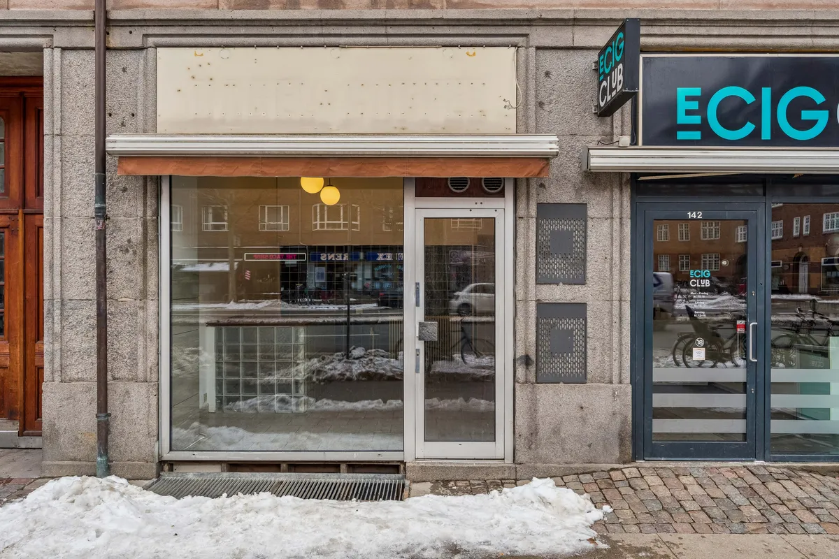 Forretningslokaler med glasfront og åbne døre på Østerbrogade 142 i København Ø. Lejemålet med 45 m² er i god stand og har lys indvendigt. Sne på gaden og refleksioner i vinduet.