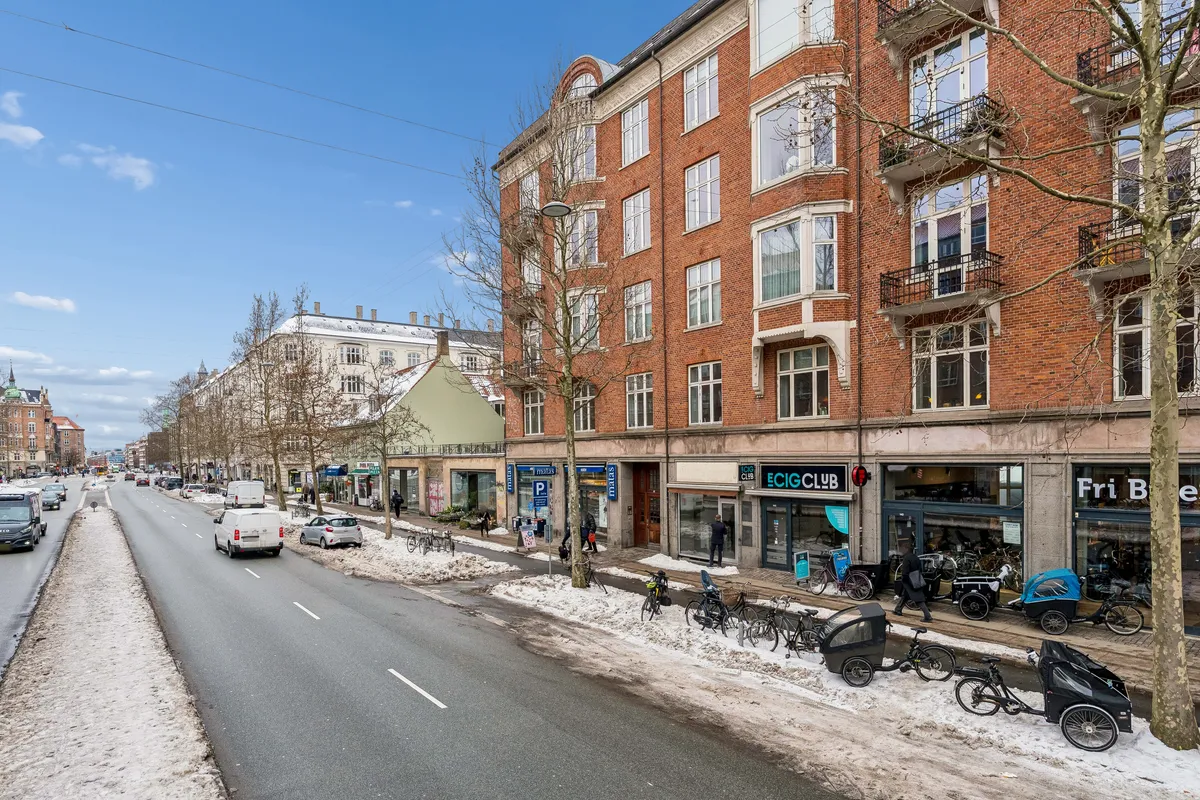 Butik på Østerbrogade 142 i København med snedækket og cykler udenfor. Lejemålet er fordelt på to etager og er ca. 45 m² stort. Der er gadebelysning og flere biler parkeret langs gaden.