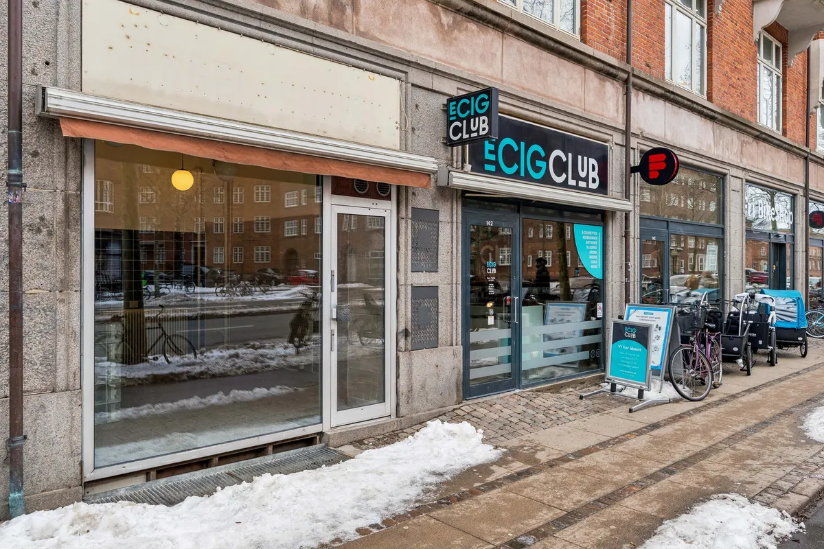 Butik med vinduer i glas og rødt skjold med teksten E-CIG Club, samt et cykelstativ med en cykel og to vogne på fortovet med sne