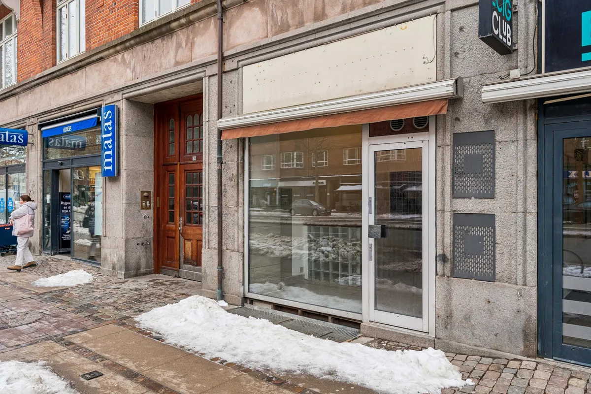 En kvinde går forbi en lejlighedsdør på Østerbrogade, og der er sne liggende på fortovet, mens der er skilte på facaden