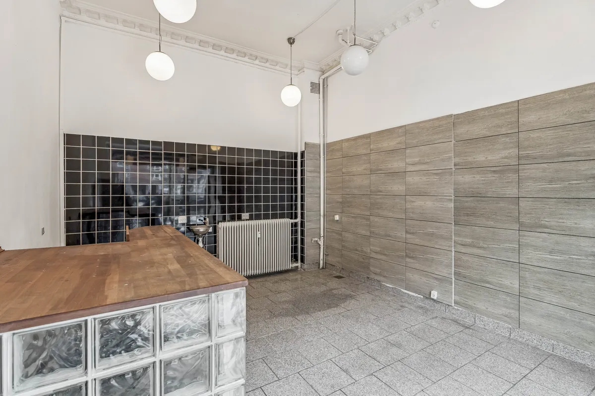 Lukket lejemål med køkkenbord og moderne lysekroner, to tømmerkister og hvidt og sort fliser på væggen.