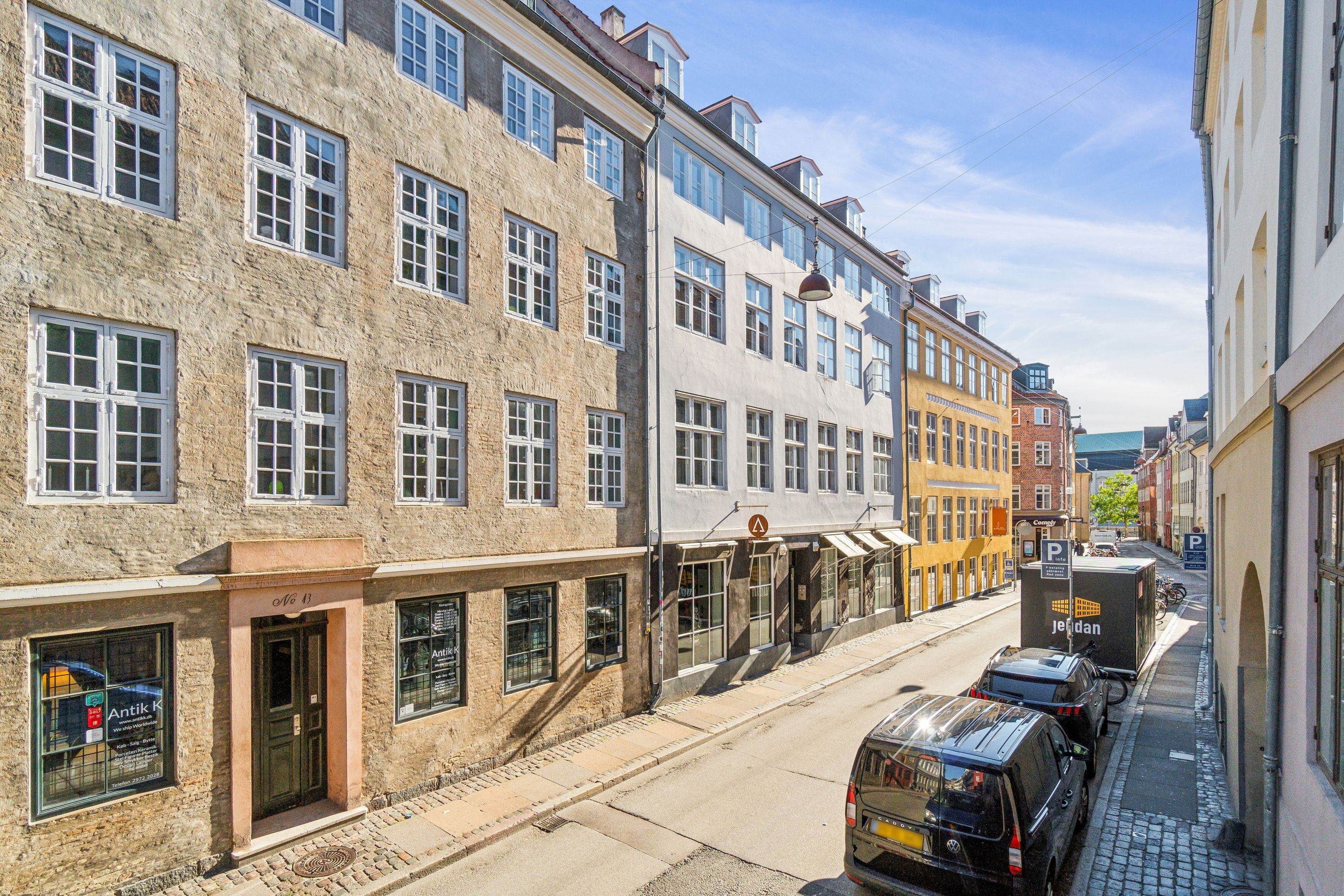 Kontorbyggeri med højstandigt gulv og moderne vinduer, hvor biler er parkeret langs gaden og en lagervogn står foran.