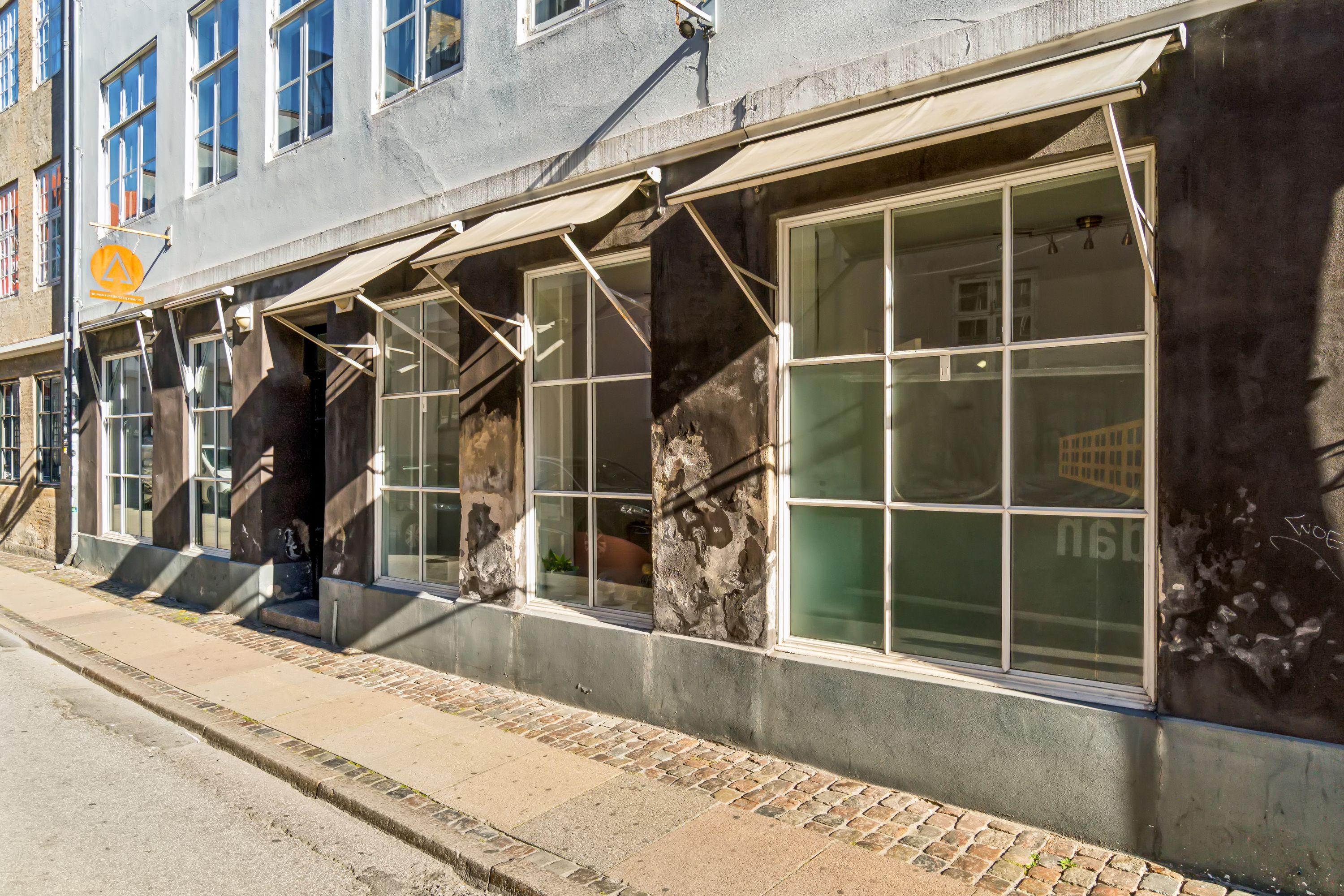 Kontor til leje i Knabrostræde, 1210 København K. Store vinduer med skyggekast og lysegardiner, og graffiti på facaden
