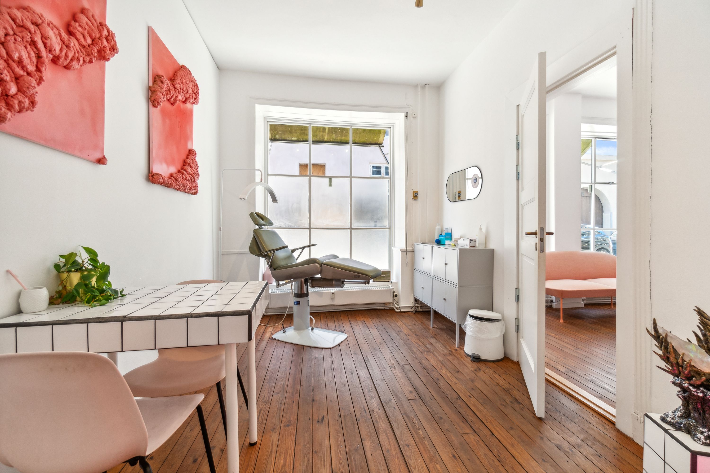 Kontor med elegant indretning og højloft, hvor en lægestol og bord med puder venter på besøgende. Dekorativt gulv og farverige vægmalerier.