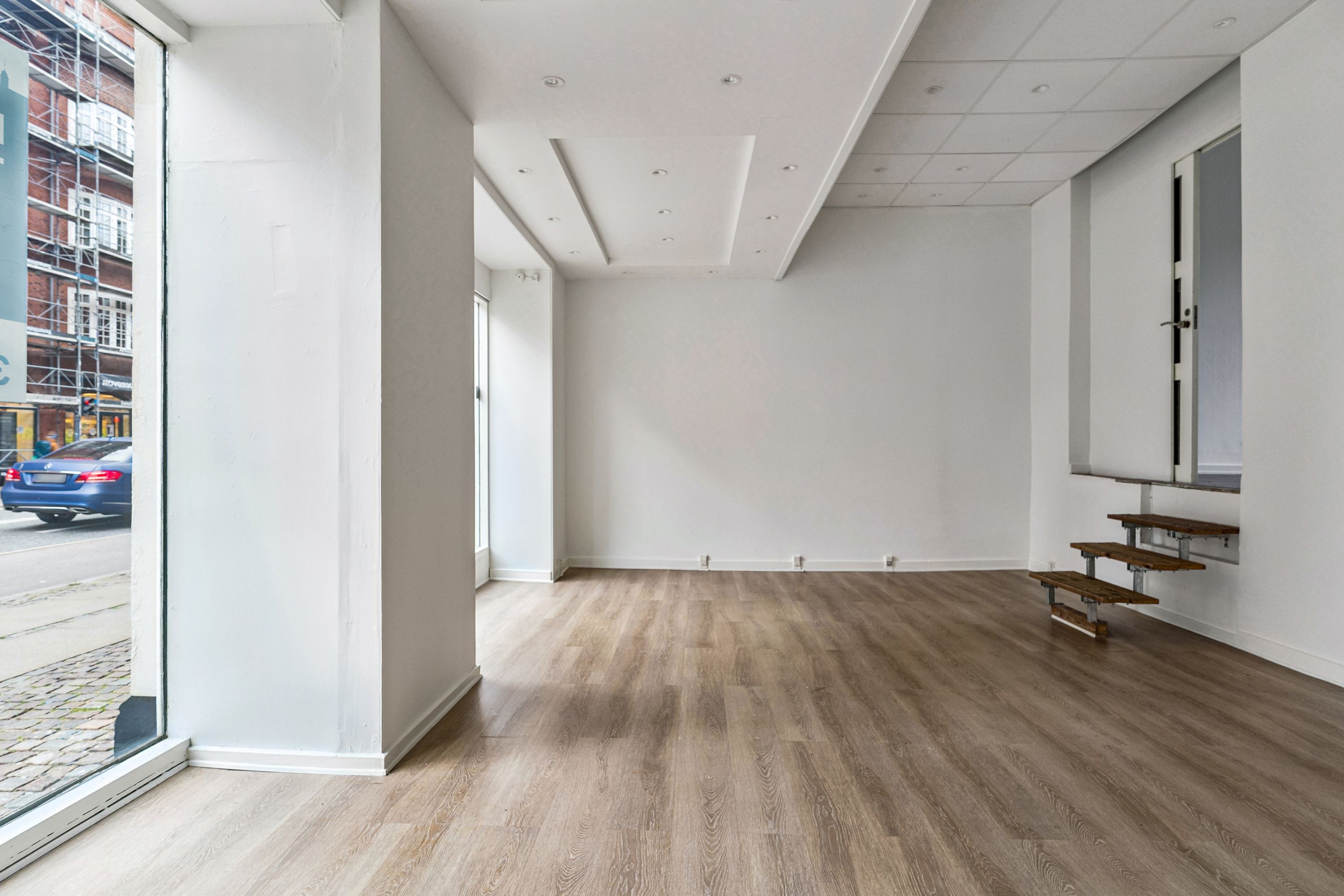 Store lyst salgslokale med trægulv og to store facadevinduer mod Amagerbrogade og en trappe til et lagerrum