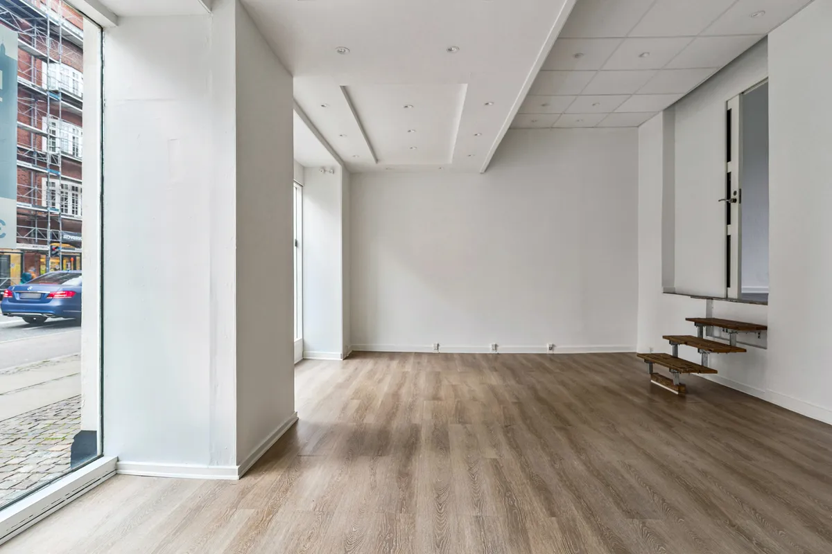 Store lyst salgslokale med trægulv og to store facadevinduer mod Amagerbrogade og en trappe til et lagerrum