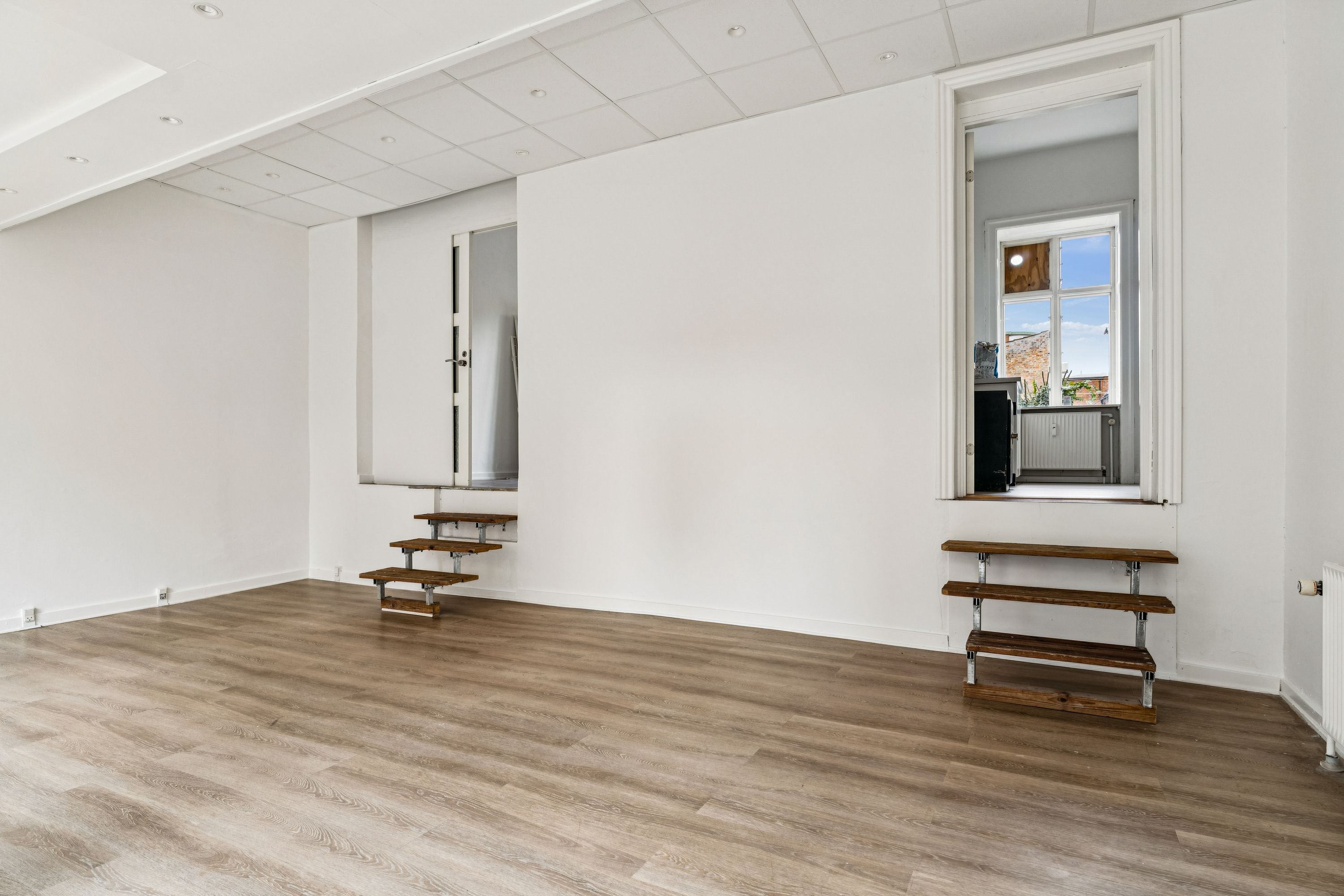 Lyst salgslokale med moderne indretning og lysegule gulvbelægning, højt til loftet, lyse facadevinduer og lysetak med indbyggede lysekroner