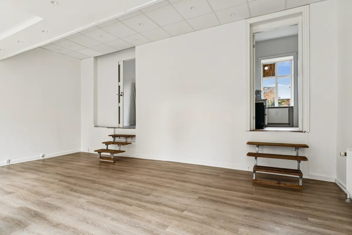 Lyst salgslokale med moderne indretning og lysegule gulvbelægning, højt til loftet, lyse facadevinduer og lysetak med indbyggede lysekroner