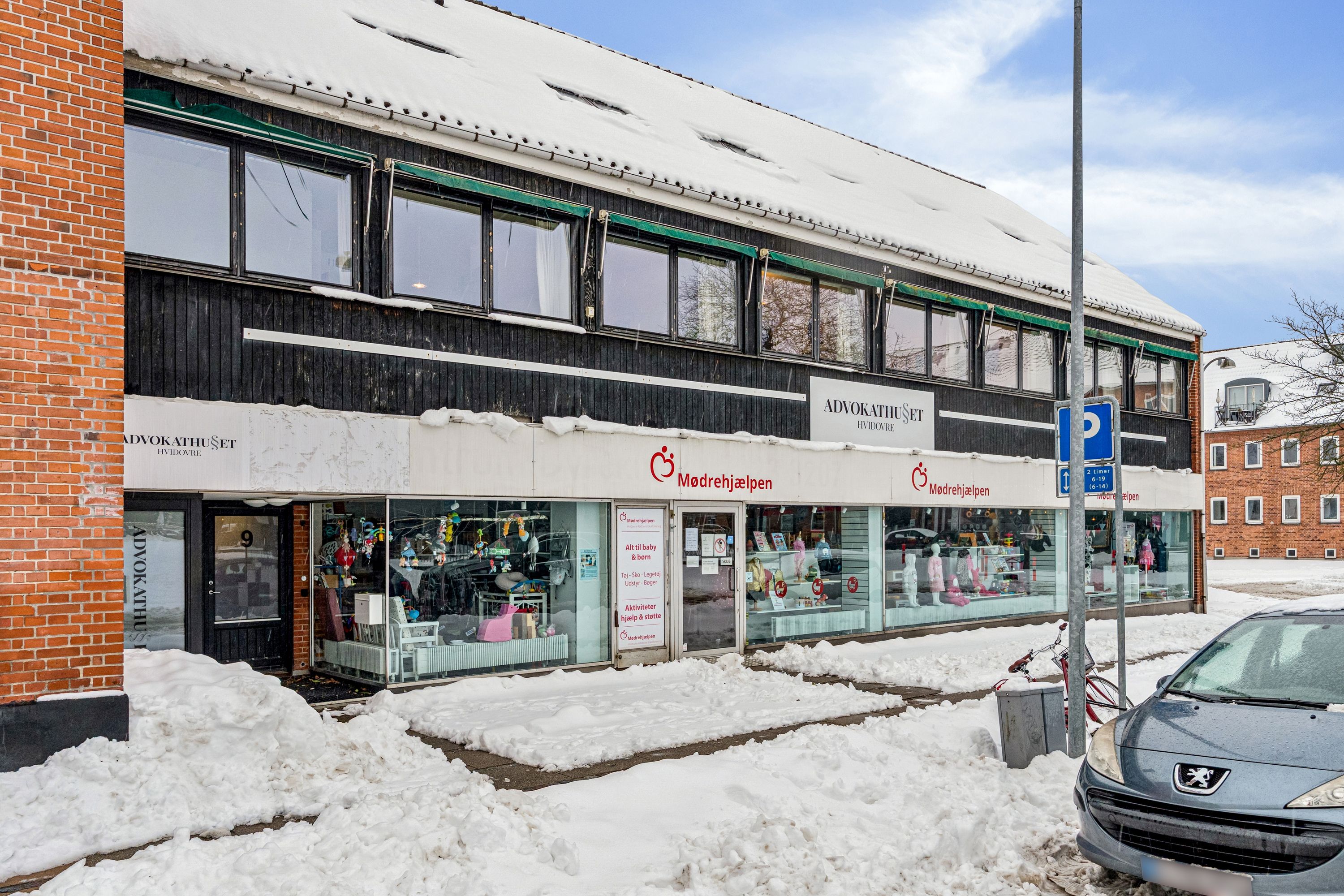 Kontorbyggerne i røde mursten og snehvidt tag, mødrehjælpen og advokathuset på Hvidovre Torv med sne på fortovet og en Peugeot parkeret ved siden af