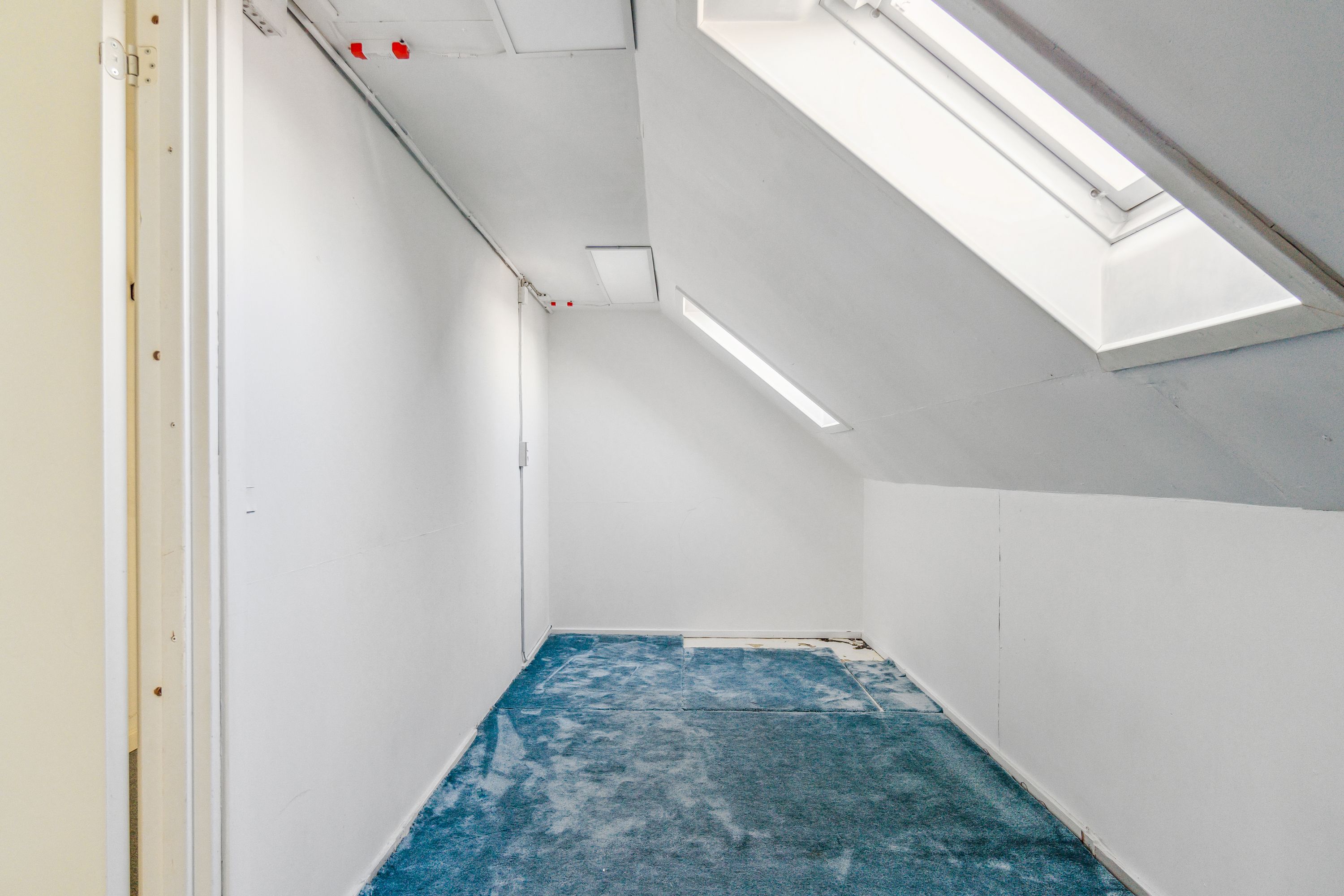 Kontorrum med hvid væg og blå gulv og loft med to loftsvinduer og indbyggede lys.