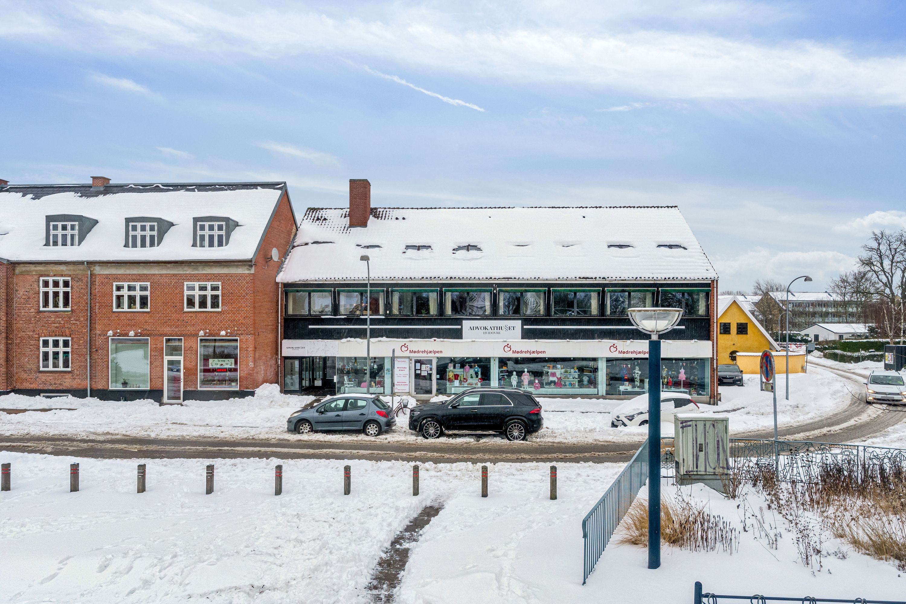 Kontorlokationer i Hvidovre med udsigt over torv og hyggelige butikker og caféer, med to biler parkeret i sne, og to lysstofhøje lysstofter på hjørnet