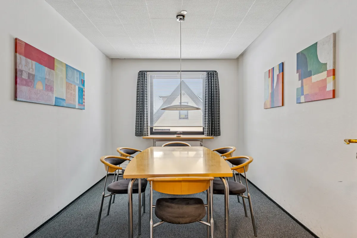 Moderne mødelokale med lysegul tavle og lysegule stole samt moderne kunstværker på væggen, hvor vinduet er dekoreret med gardiner og vinduesrude.