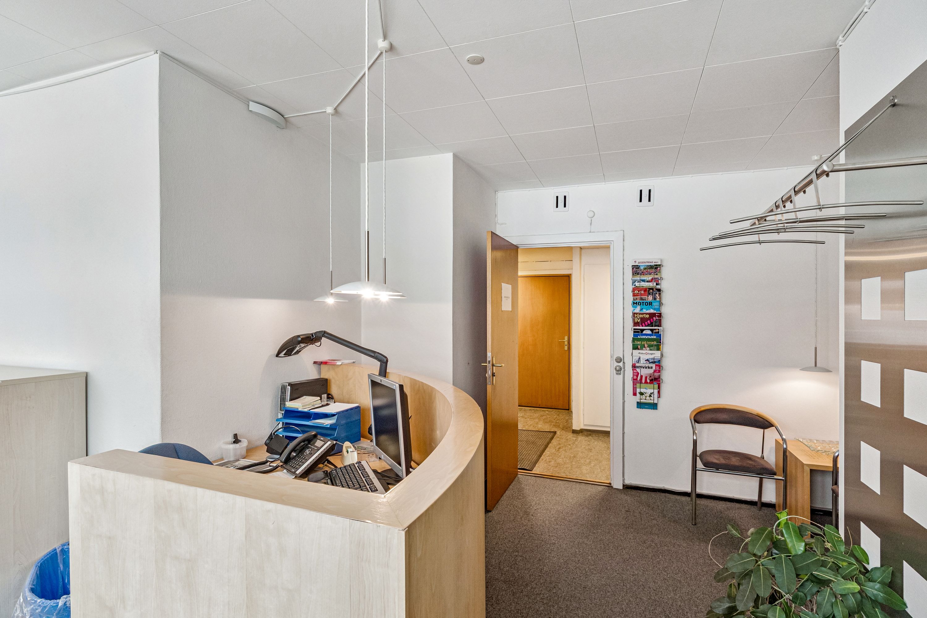 Kontor med indvendig reception, computer og telefon på skrivebordet, og stole samt bøfler til hængning på væggen