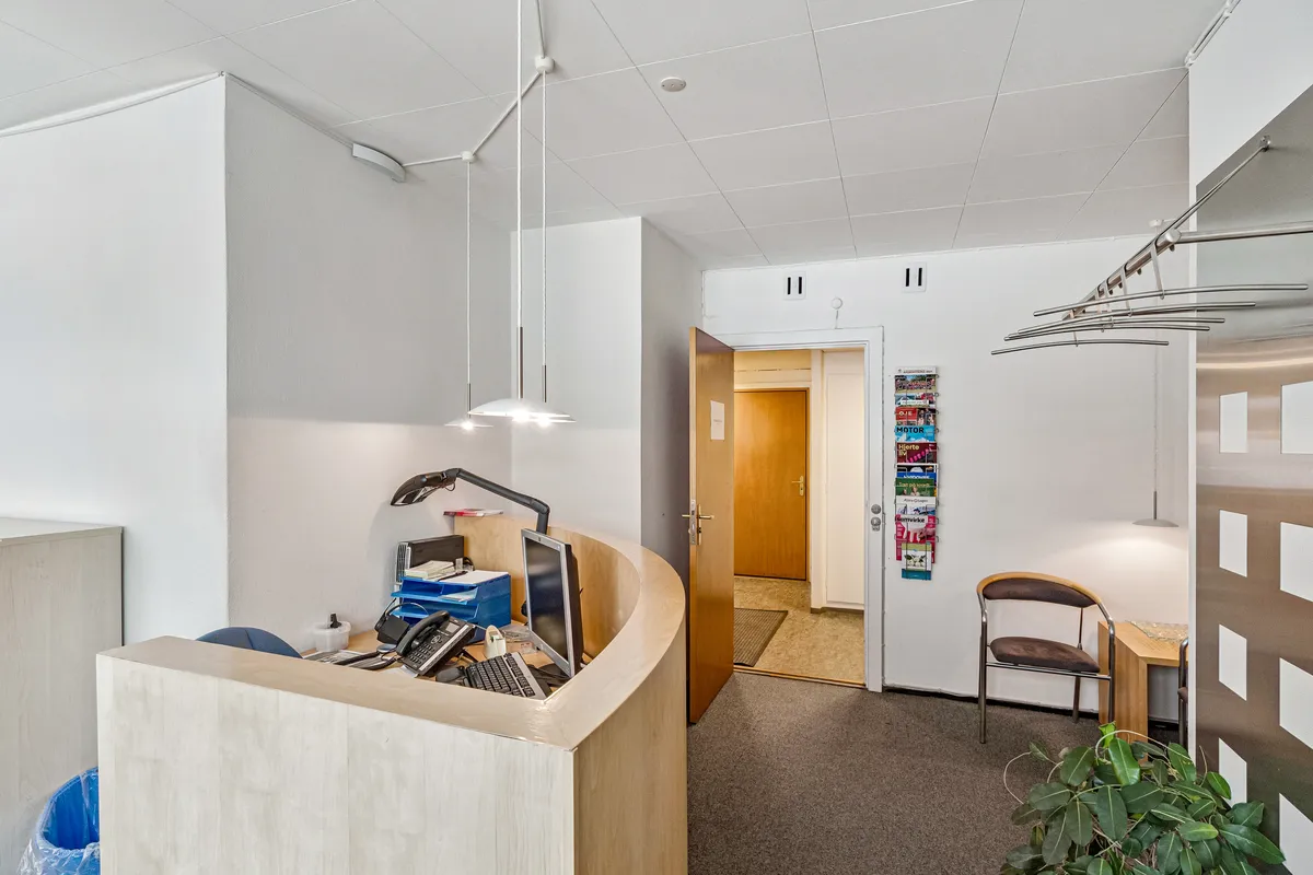 Kontor med indvendig reception, computer og telefon på skrivebordet, og stole samt bøfler til hængning på væggen