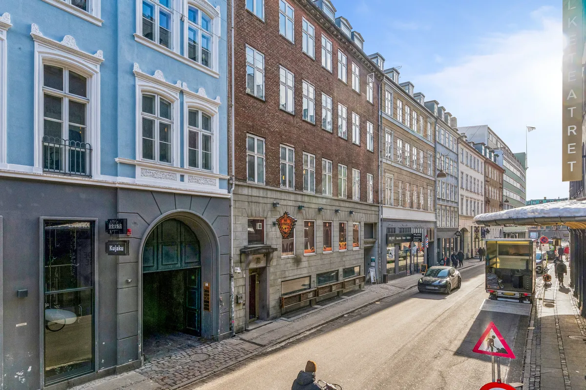 På Nørregade i København ligger et kontorlokal med mange vinduer og lyse interiører. Folk går på fortovet og biler kører langs gaden. Værelset har tekster og skilte på flere sprog.