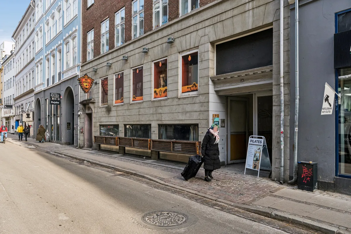 En kvinde går med kuffert og håndtaske foran Nørregade 26. Kontoret har moderne møbler og lyse vinduer med udsigt til gaden.