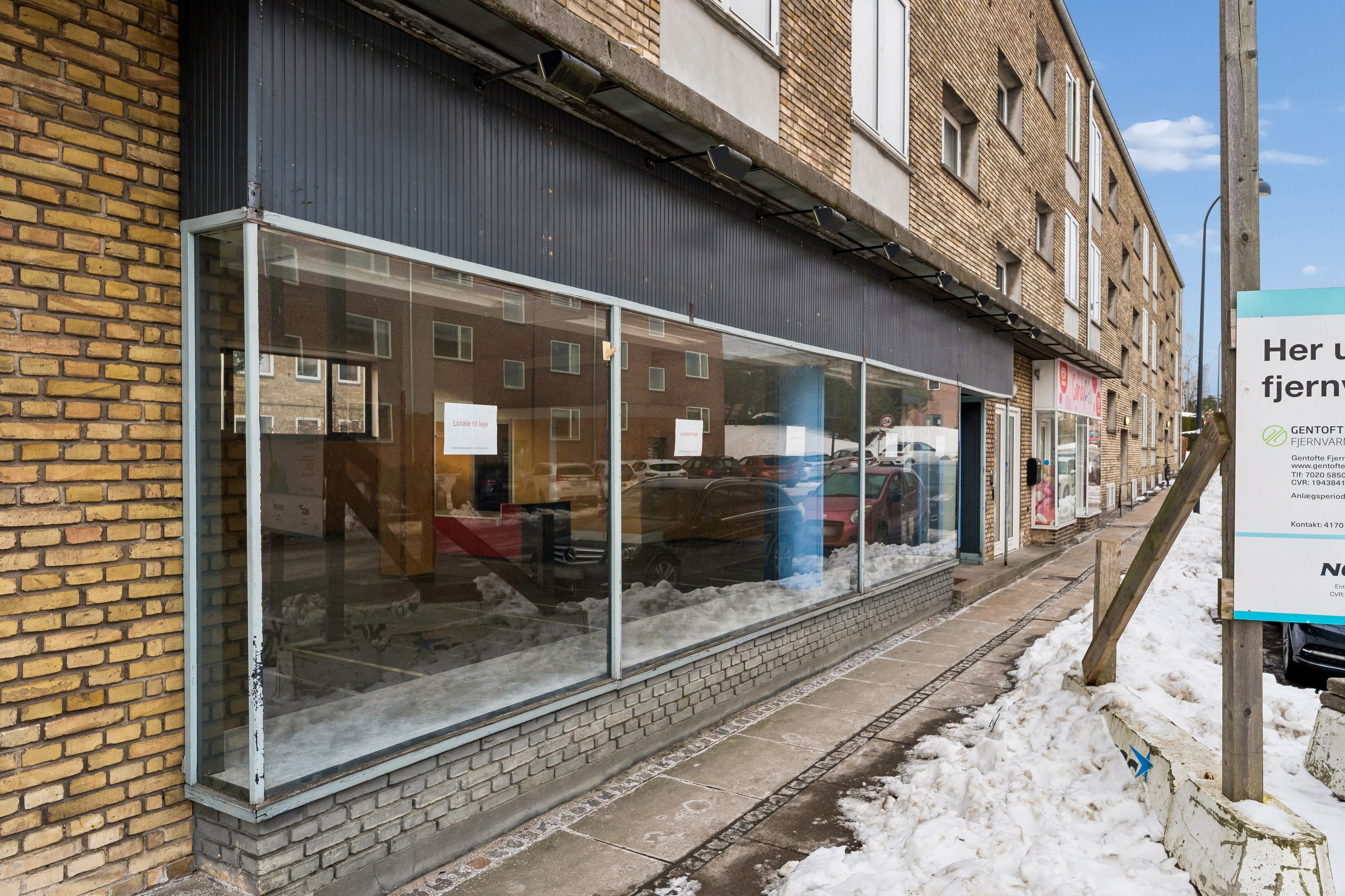 Byggegrund med glasfacade og snedækket foran. Snegløsset, glasdækket lokal med skilte og snedækket fortov.