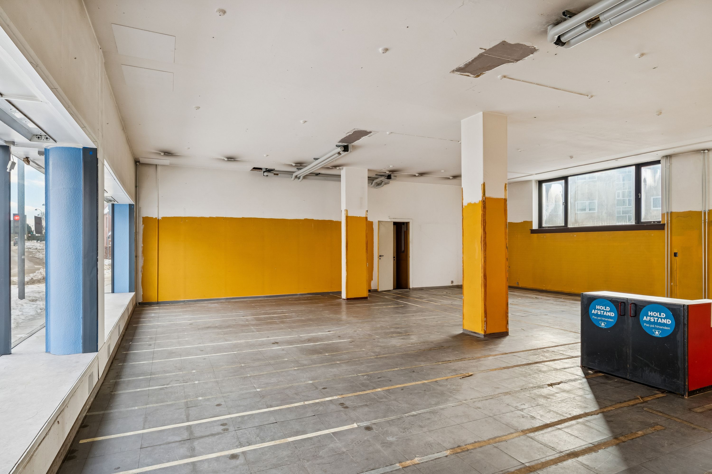 Store tomte med gul og hvid væg, højt loft med lysekroner, møbleret skranken og gule og blå søjler