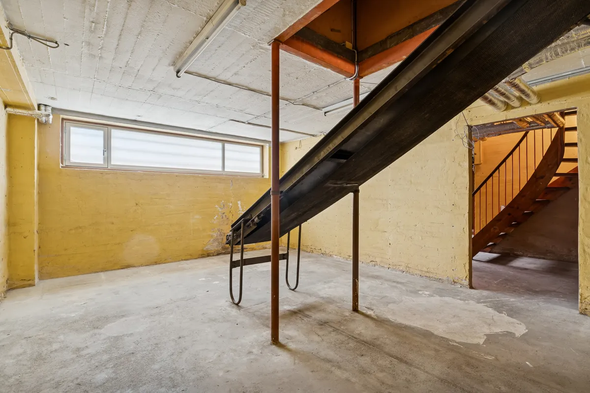 Lager med metalkonstruktioner og stige til loftsrummet. Gulv, vægge og loft er gule. Der er en vinduesåbning i den ene væg.