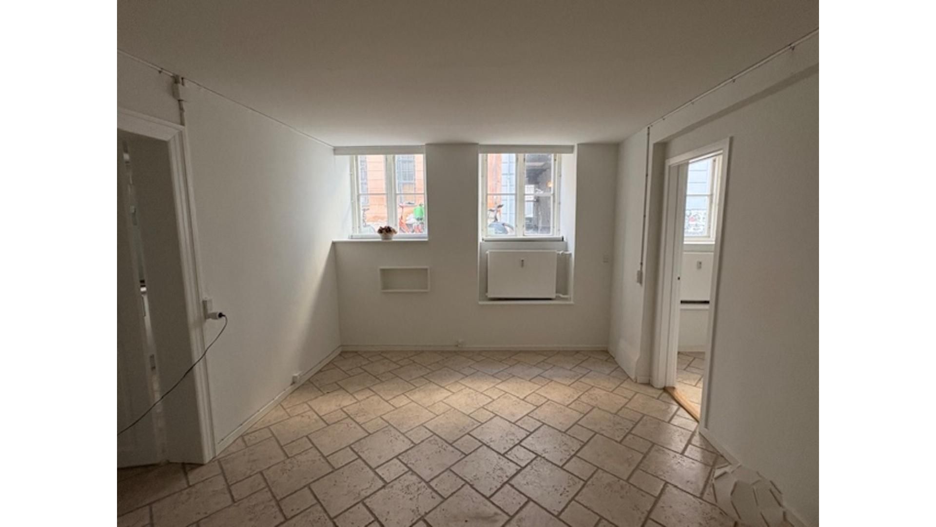 et rum med hvide vægge og gulv, to vinduer og to døre, der fører ind og ud af rummet