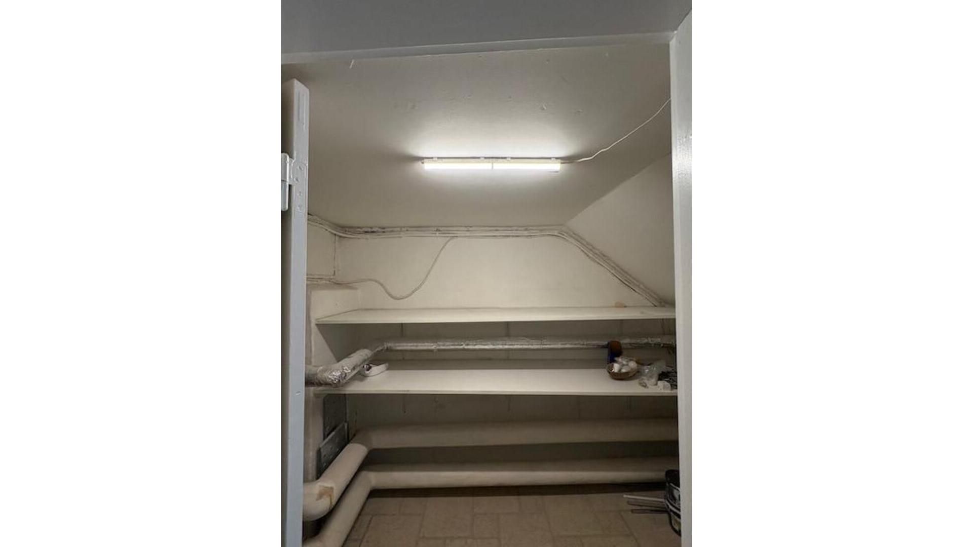 Et loftsrum med hvide vægge og loft. Værelset har tre højdejusterede hylder og en lysebue, som er tændt.